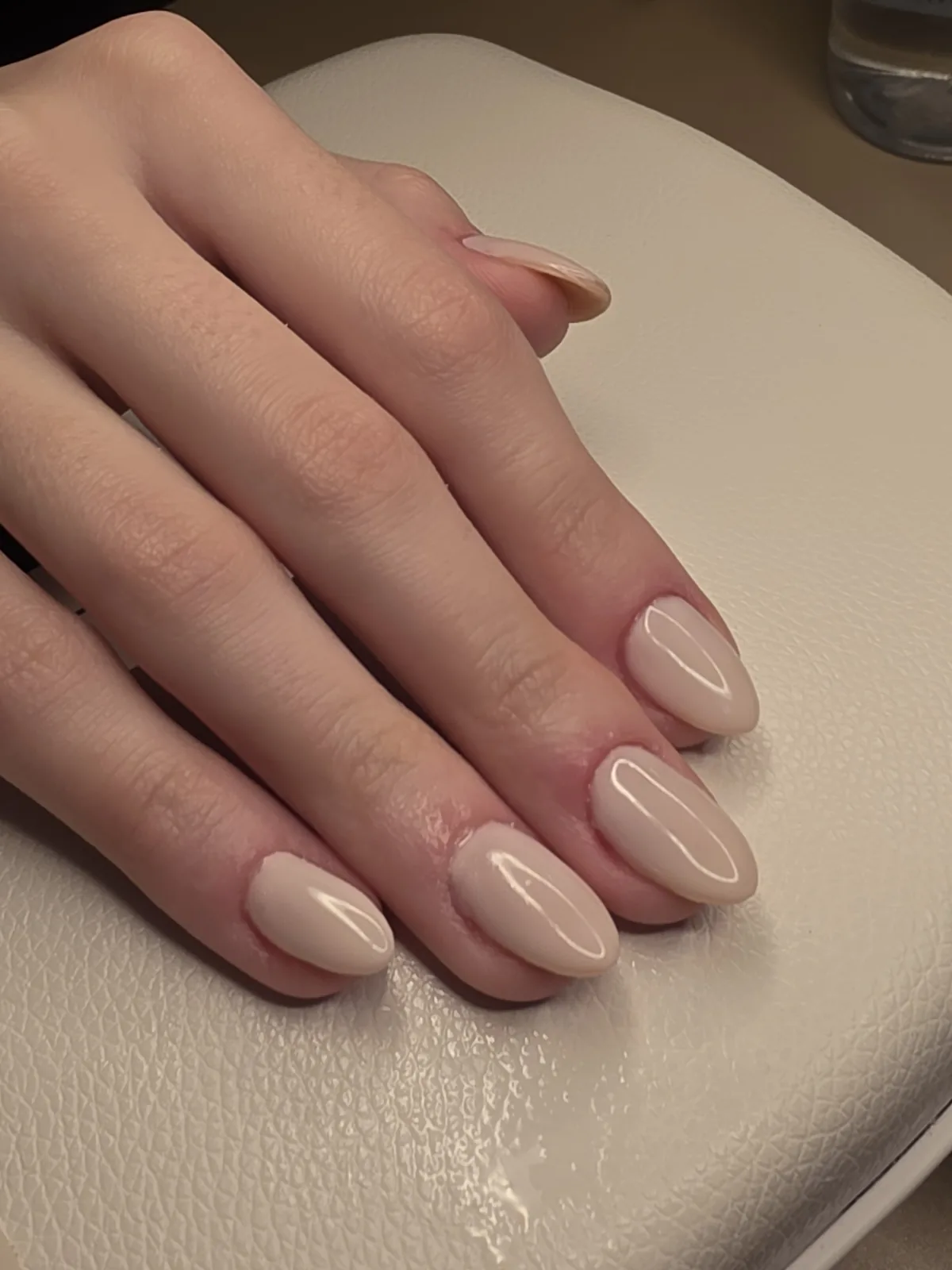 Mão com esmaltação em gel nude bege em unhas amendoadas, apoiada sobre a cabine O NAIL no estúdio em Jundiaí