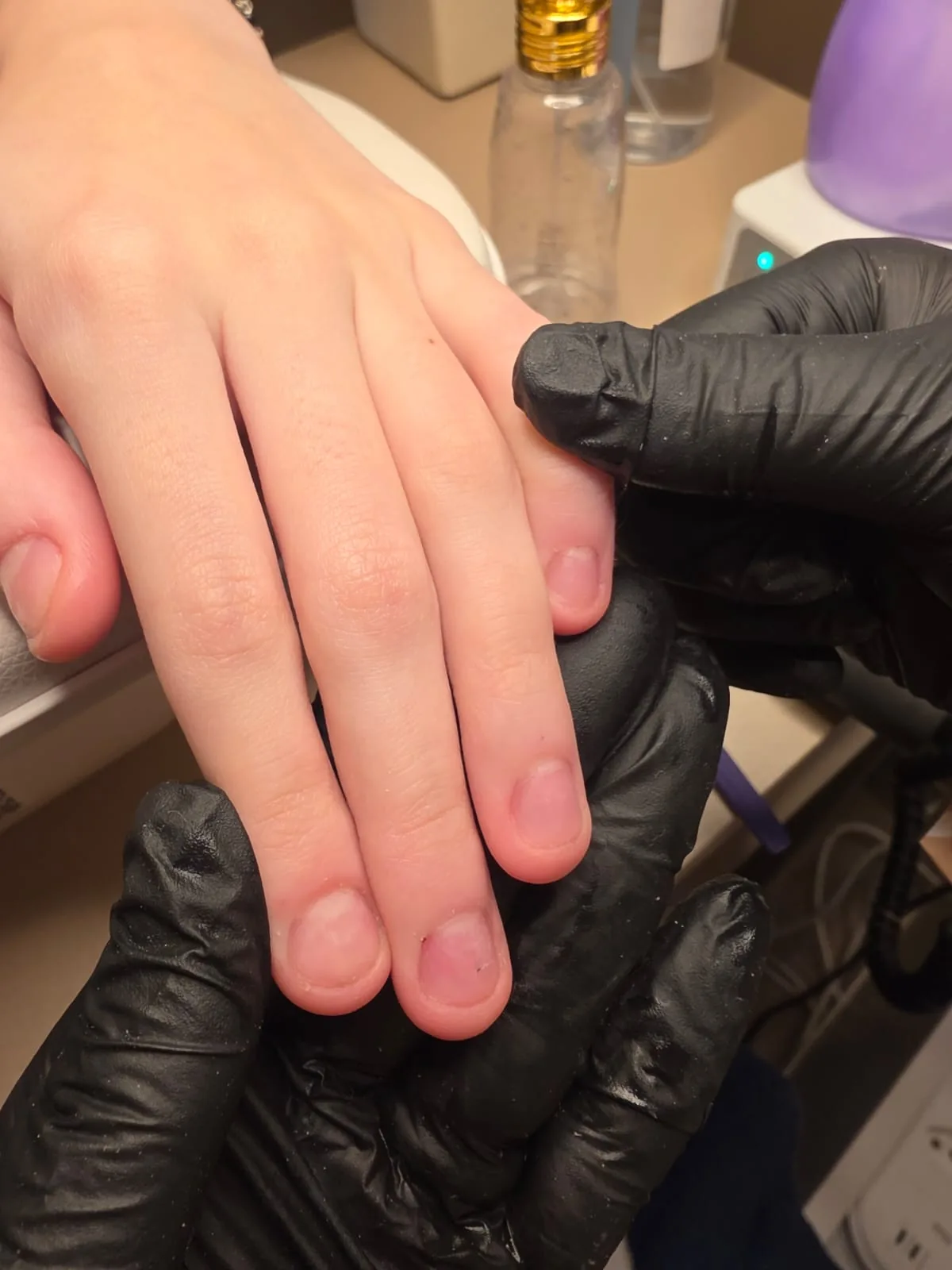 Profissional de luvas pretas segurando a mão da cliente durante o preparo das unhas na bancada do estúdio em Jundiaí