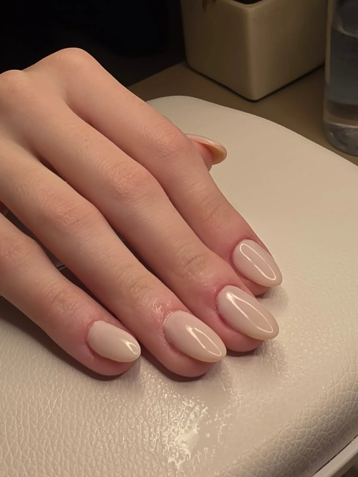 Esmaltação em gel nude leitoso em unhas amendoadas, com a mão da cliente sobre o apoio de braço O NAIL no estúdio em Jundiaí