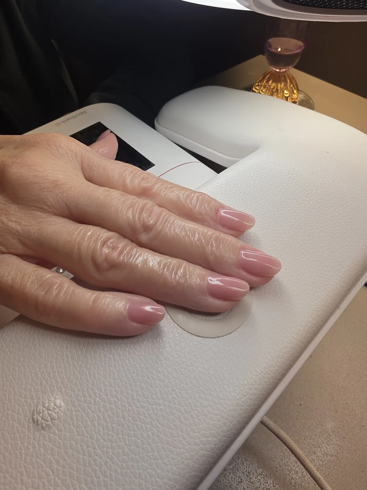Mão com esmaltação em gel nude apoiada na cabine O NAIL, logo após a secagem, no estúdio em Jundiaí