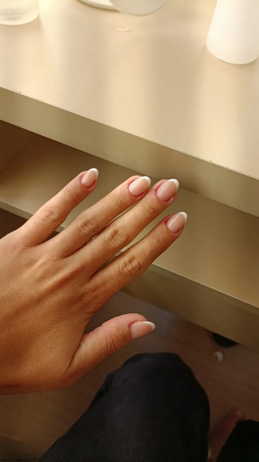 Mão com unhas amendoadas longas, francesinha fina sobre base nude, apoiada na bancada