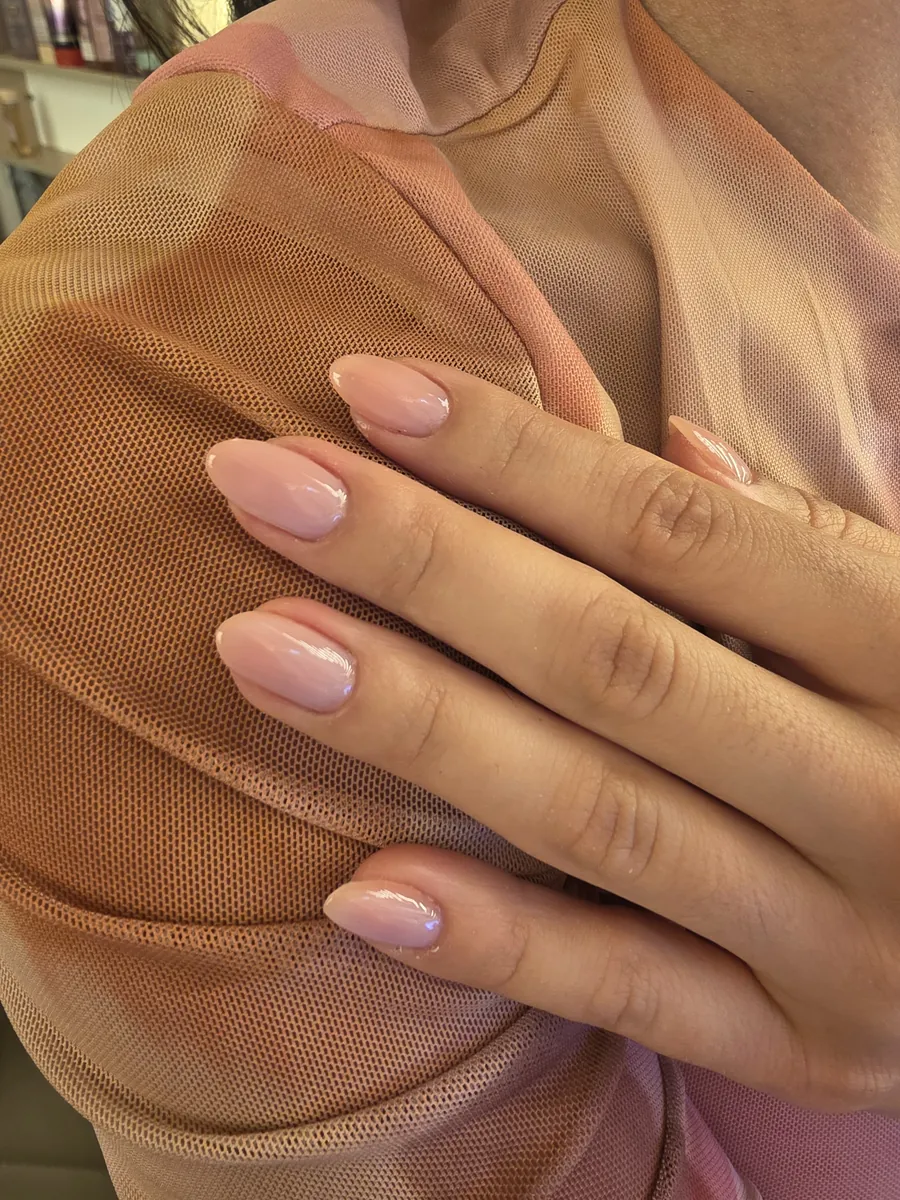 Unhas amendoadas em rosa-nude translúcido com brilho alto, mão apoiada no ombro